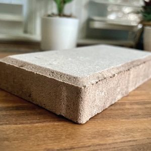 May include: A light brown rectangular brick with a smooth, light gray top surface. The brick has a slightly rough texture on the sides.