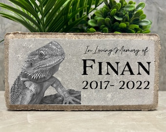 May include: A gray concrete memorial block with a black and white drawing of a bearded dragon. The text "In Loving Memory of FINAN 2017-2022" is printed on the block.