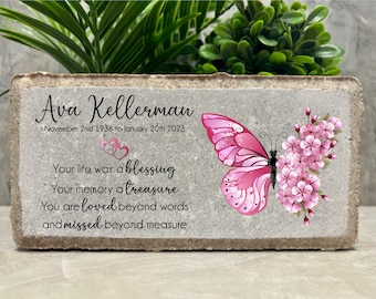 Può includere: Una pietra commemorativa in cemento grigio con una farfalla rosa e fiori rosa. La pietra ha il testo "Ava Kellerman, 2 novembre 1936 al 20 gennaio 2023, La tua vita è stata una benedizione, Il tuo ricordo un tesoro, Sei amata oltre le parole e manchi oltre ogni misura."