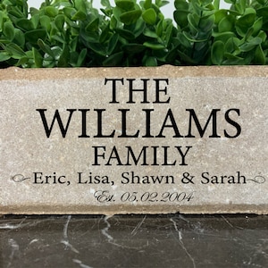 May include: A light brown rectangular stone with the text "THE WILLIAMS FAMILY Eric, Lisa, Shawn & Sarah Est. 05.02.2004" engraved in black.