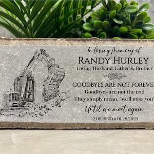 May include: A gray concrete memorial block with a black and white illustration of an excavator. The text reads "In loving memory of Randy Hurley, Loving Husband, Father & Brother, Goodbyes are not forever, Goodbyes are not the end, They simply mean, "we'll miss you", Until we meet again, 12.08.1935 to 01.28.2023".