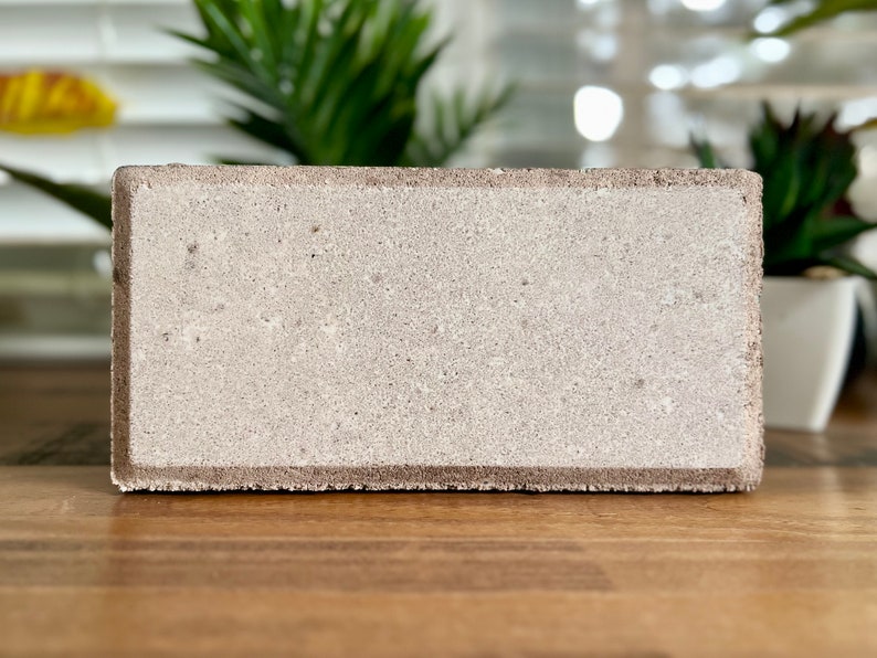 May include: A light gray concrete block with a rough texture. The block is rectangular and has a slightly rounded edge.