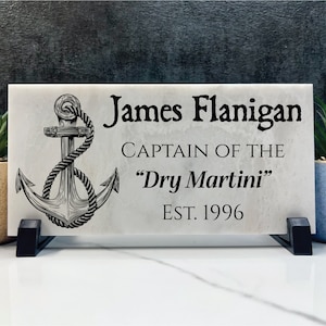 May include: A white marble plaque with a black anchor and rope design. The plaque reads "James Flanigan, Captain of the "Dry Martini" Est. 1996".