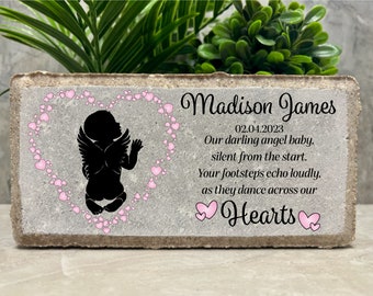 Può includere: Un blocco commemorativo in cemento grigio con un motivo a cuore rosa e una silhouette di un bambino angelo. Il testo recita "Madison James 02.04.2023 Il nostro caro angioletto. silenzioso fin dall'inizio. I tuoi passi risuonano forte. mentre danzano attraverso i nostri cuori"