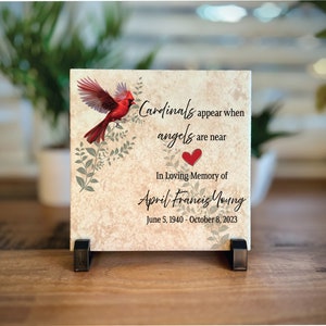 May include: A ceramic tile with a red cardinal bird and green leaves. The tile has the text "Cardinals appear when angels are near" and "In Loving Memory of April Francis Young June 5, 1940 - October 8, 2023".