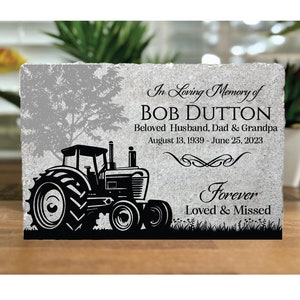 May include: A gray stone memorial with a black silhouette of a tractor. The text reads "In Loving Memory of BOB DUTTON Beloved Husband, Dad & Grandpa August 13, 1939 - June 25, 2023 Forever Loved & Missed"