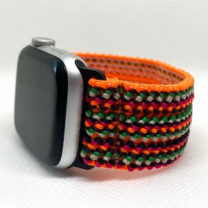 May include: A silver Apple Watch with a bright orange, green, pink, and black woven band.