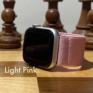 Puede incluir: Un Apple Watch plateado con una banda deportiva rosa claro. El reloj está sobre una superficie de madera.