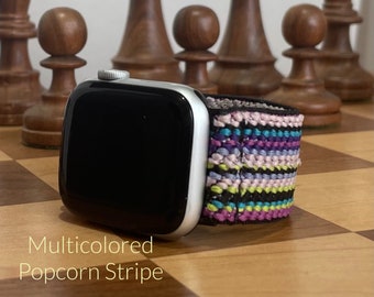May include: A silver smartwatch with a black screen and a multicolored popcorn stripe watch band. The band features a pattern of pink, purple, blue, yellow, and black stripes. The text "Multicolored Popcorn Stripe" is visible.