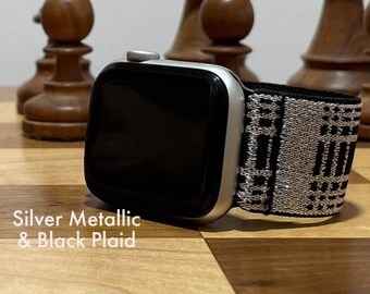 May include: A silver metallic Apple Watch with a black and white plaid sport band. The watch is on a wooden chessboard.
