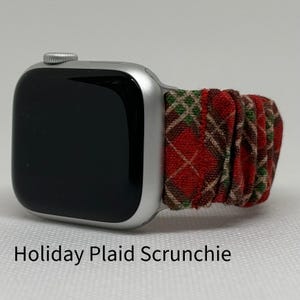 May include: A silver Apple Watch with a red, green, and brown plaid scrunchie band. The band is made of fabric and has a gathered look. The text "Holiday Plaid Scrunchie" is written below the watch.