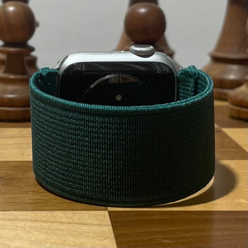 May include: A dark green sport band for an Apple Watch. The band is made of a soft, stretchy material and has a smooth, textured finish.