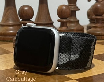 May include: A silver Apple Watch with a grey camouflage sport band. The watch is on a wooden chessboard.