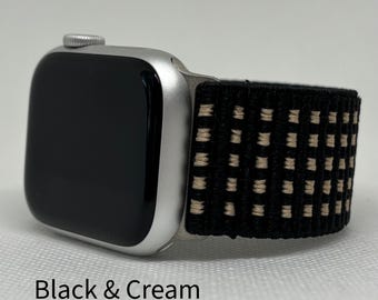 Puede incluir: Un reloj inteligente plateado con pantalla negra y una correa tejida en negro y crema. La correa presenta un patrón repetitivo de cuadrados color crema sobre fondo negro. El texto "Black & Cream" es visible en la parte inferior.