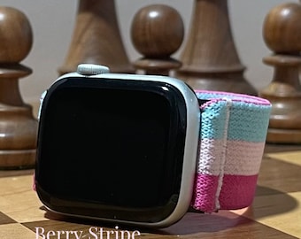 May include: A white Apple Watch with a black screen and a pink, white and blue striped sport band. The band has the text "Berry Stripe" printed on it.