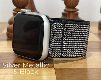 May include: A silver Apple Watch with a black and silver woven sport band. The watch is on a wooden surface.