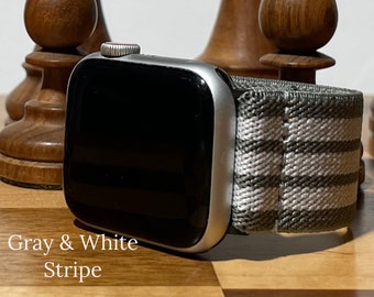 May include: A silver Apple Watch with a gray and white striped sport band. Gray & White Stripe.