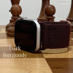 May include: A silver Apple Watch with a dark burgundy sport band. The watch is on a wooden chessboard.