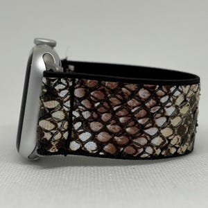 May include: A silver smartwatch with a snakeskin patterned strap. The strap has a repeating pattern of brown, tan, and white scales. The strap is attached to the watch face with a black border.