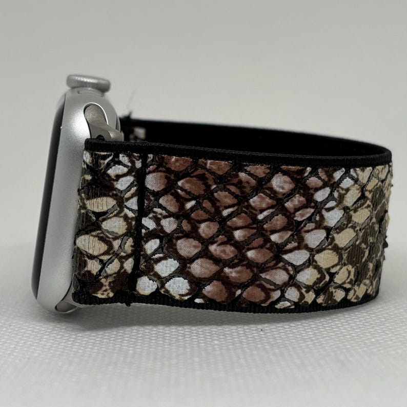 May include: A silver smartwatch with a snakeskin patterned strap. The strap has a repeating pattern of brown, tan, and white scales. The strap is attached to the watch face with a black border.
