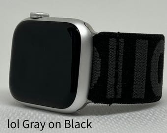 May include: A silver Apple Watch with a black and grey patterned sport band. The band has the word "lol" printed on it in grey.