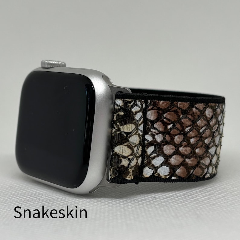 May include: A silver smartwatch with a black screen and a snakeskin patterned strap. The strap features a brown, tan, and white design. The word "Snakeskin" is printed at the bottom of the image.