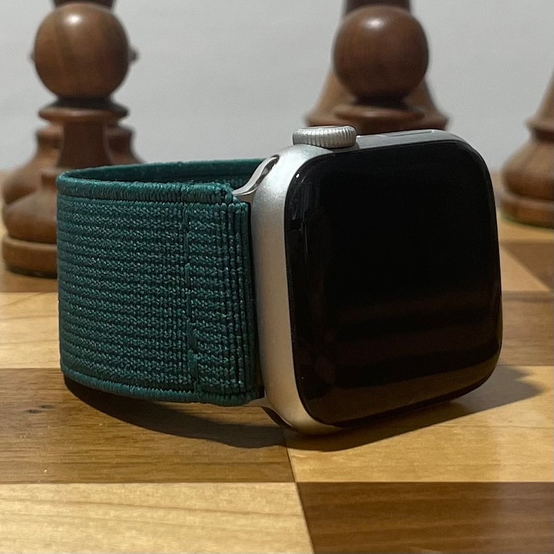 May include: A silver Apple Watch with a dark green sport band. The watch is on a wooden surface.