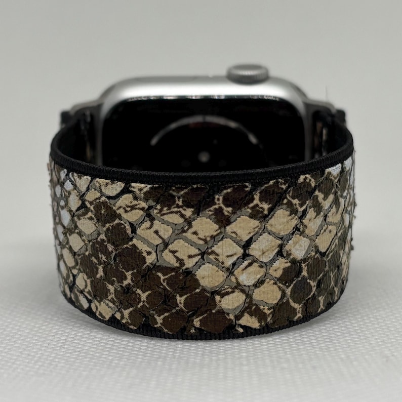 May include: A silver smartwatch with a snakeskin-patterned band in shades of brown, tan, and white. The band is wrapped around the watch face, showcasing the textured design. The band is approximately 2.5 cm wide.