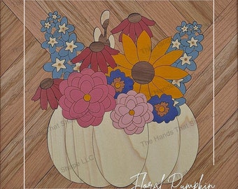 May include: A wooden pumpkin with a floral arrangement inside. The flowers are pink, yellow, blue, and red. The pumpkin is painted white and has the words "The Hands That Shape LLC" and "Floral Pumpkin" written on it.