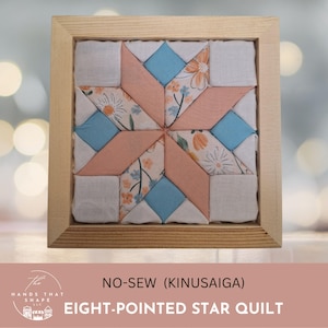 May include: A square wooden frame containing a no-sew Kinusaiga eight-pointed star quilt block. The design features fabric pieces in solid white, solid light blue, and a floral print with orange and blue flowers on a white background.