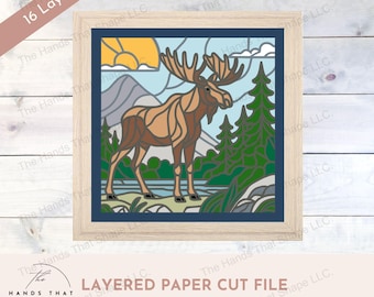 Puede incluir: Un archivo de corte de papel en capas que representa un alce de pie en un bosque con un lago y montañas en el fondo. El diseño está en estilo de vitral con una variedad de colores, incluyendo marrón, verde, azul y amarillo. El archivo está disponible en formatos SVG, DXF y EPS.