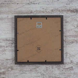 The back side of the layered cardstock paper shadow box that uses sheets of paper to create a 3d image. The backside shows The Hands That Shape, LLC logo and mounted hanger.
