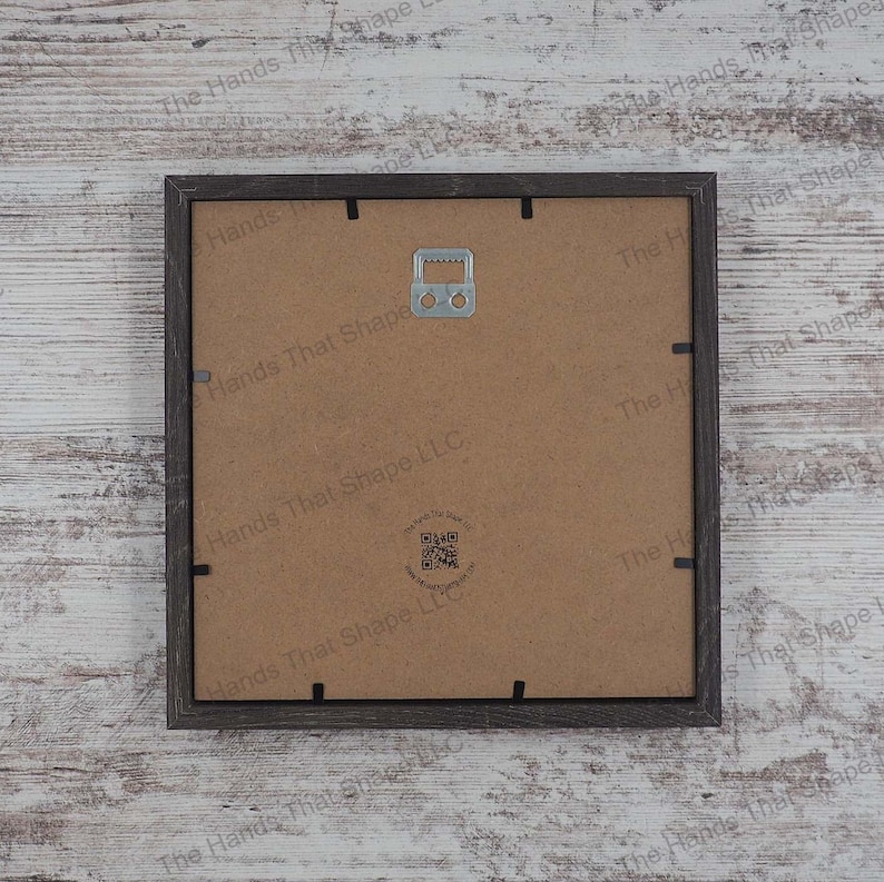 The back side of the layered cardstock paper shadow box that uses sheets of paper to create a 3d image. The backside shows The Hands That Shape, LLC logo and mounted hanger.