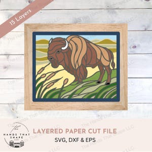 Könnte beinhalten: Eine mehrschichtige Papierschnittdatei mit einem braunen Bison, der auf einer grünen Wiese steht. Das Design ist in einem Holzrahmen gerahmt und enthält den Text "Layered Paper Cut File SVG, DXF & EPS".