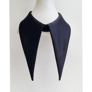 Pode incluir: Uma gola preta removível com um design pontiagudo. A gola é feita de um material liso, possivelmente acetinado, e é exibida em uma cabeça de manequim branca. A forma da gola é um estilo clássico e elegante.