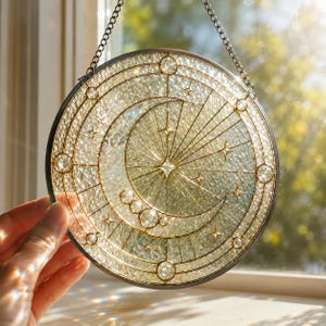 Könnte beinhalten: Ein runder Sonnenfänger aus Buntglas mit einem Halbmond- und Sternenmotiv, bestehend aus strukturierten, klaren Glasscheiben, die durch dünne goldene Metalllinien verbunden sind. Das Objekt ist an einer Metallkette aufgehängt.