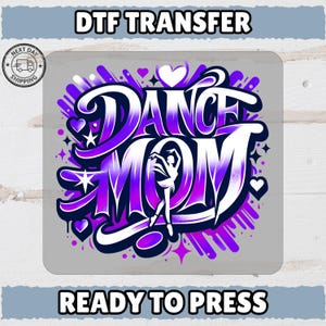May include: A DTF transfer design with the words "DANCE MOM" in a graffiti-style font, featuring a ballerina silhouette. The design is in shades of purple and white, with hearts and stars. The text "READY TO PRESS" is at the bottom.
