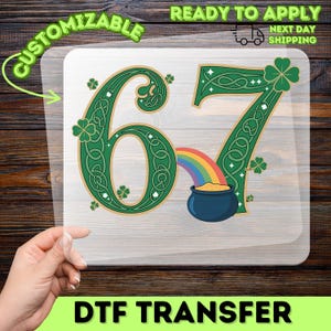 May include: A clear DTF transfer sheet featuring the number 67 in green with Celtic knot designs and shamrocks. A rainbow leads to a pot of gold. The words "Customizable" and "Ready to Apply" are also visible.