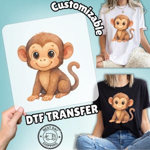 May include: A brown monkey illustration with large eyes and a smiling expression is featured on a white background. The image is labeled "Customizable" and "DTF TRANSFER". The image is shown on a white and black t-shirt.