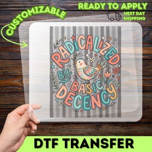 May include: A rectangular DTF transfer sheet featuring a gray and white striped background with a central illustration of a bird. The text RADICALIZED BY BASIC DECENCY is printed in colorful, rounded lettering around the bird, surrounded by small floral and star accents.