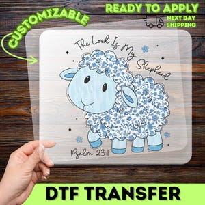 May include: A DTF transfer featuring a light blue sheep illustration with floral accents. The text "The Lord Is My Shepherd" and "Psalm 23:1" are included. The words "Customizable" and "Ready to Apply" are also visible.