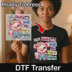 May include: A black t-shirt featuring a graphic of a cartoon pig wearing a pink headband with a flower and blue overalls, holding a pink cup. The text reads Shhhh Don't Talk Until My Cup Is Empty. A matching DTF transfer sheet is also shown.
