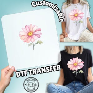 May include: A DTF transfer featuring a watercolor-style pink daisy with a yellow center and green stem. The word "Customizable" is arched above the transfer. The image also shows the design printed on white and black t-shirts.