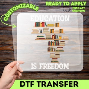May include: A DTF transfer with the words "EDUCATION IS FREEDOM" in white, with a graphic of bookshelves filled with books. The transfer is on a clear background with a wooden plank backdrop. The words "CUSTOMIZABLE" and "READY TO APPLY" are also visible.