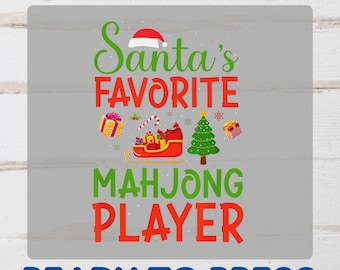 May include: A DTF transfer design with the text "Santa's Favorite Mahjong Player" in green and red. The design includes a Santa hat, a sleigh, a Christmas tree, and gift boxes. The text "READY TO PRESS" is also included.