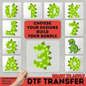 May include: A collection of green dinosaur-themed letters and numbers with a dotted pattern, displayed on individual silver squares. A red rectangle reads "CHOOSE YOUR DESIGNS BUILD YOUR BUNDLE". The phrase "READY TO APPLY DTF TRANSFER" is also visible.