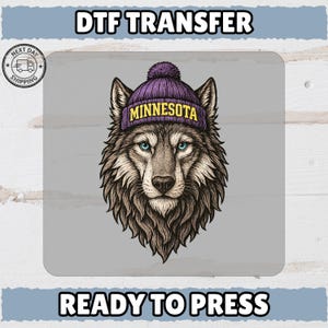 May include: A DTF transfer featuring a detailed illustration of a wolf head wearing a purple pom-pom beanie with the word MINNESOTA printed in yellow text. The wolf has brown fur, pointed ears, and bright blue eyes, set against a light gray background.
