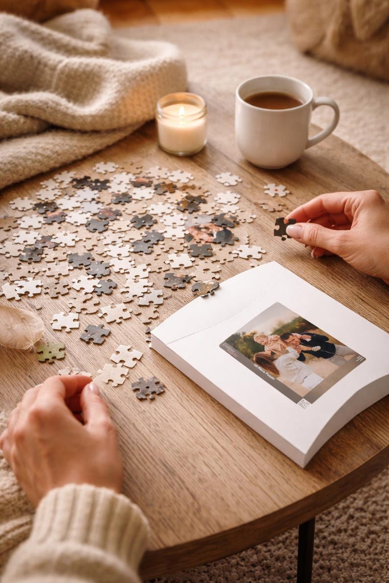 May include: A custom photo puzzle with pieces scattered on a wooden table. A white mug of coffee, a lit candle, and a folded blanket are also on the table. The puzzle's image is visible on the box.