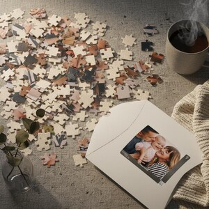 May include: A scattered jigsaw puzzle with pieces featuring family photos. A mug of coffee steams nearby, with a white envelope displaying a family portrait. A cozy blanket and small vase with greenery complete the scene.