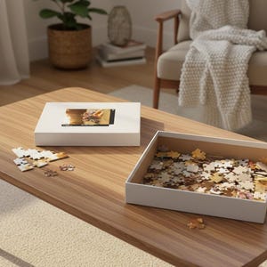 May include: A wooden coffee table holds a white puzzle box with an image on top, a box filled with puzzle pieces, and a few scattered pieces. The scene suggests a leisure activity.